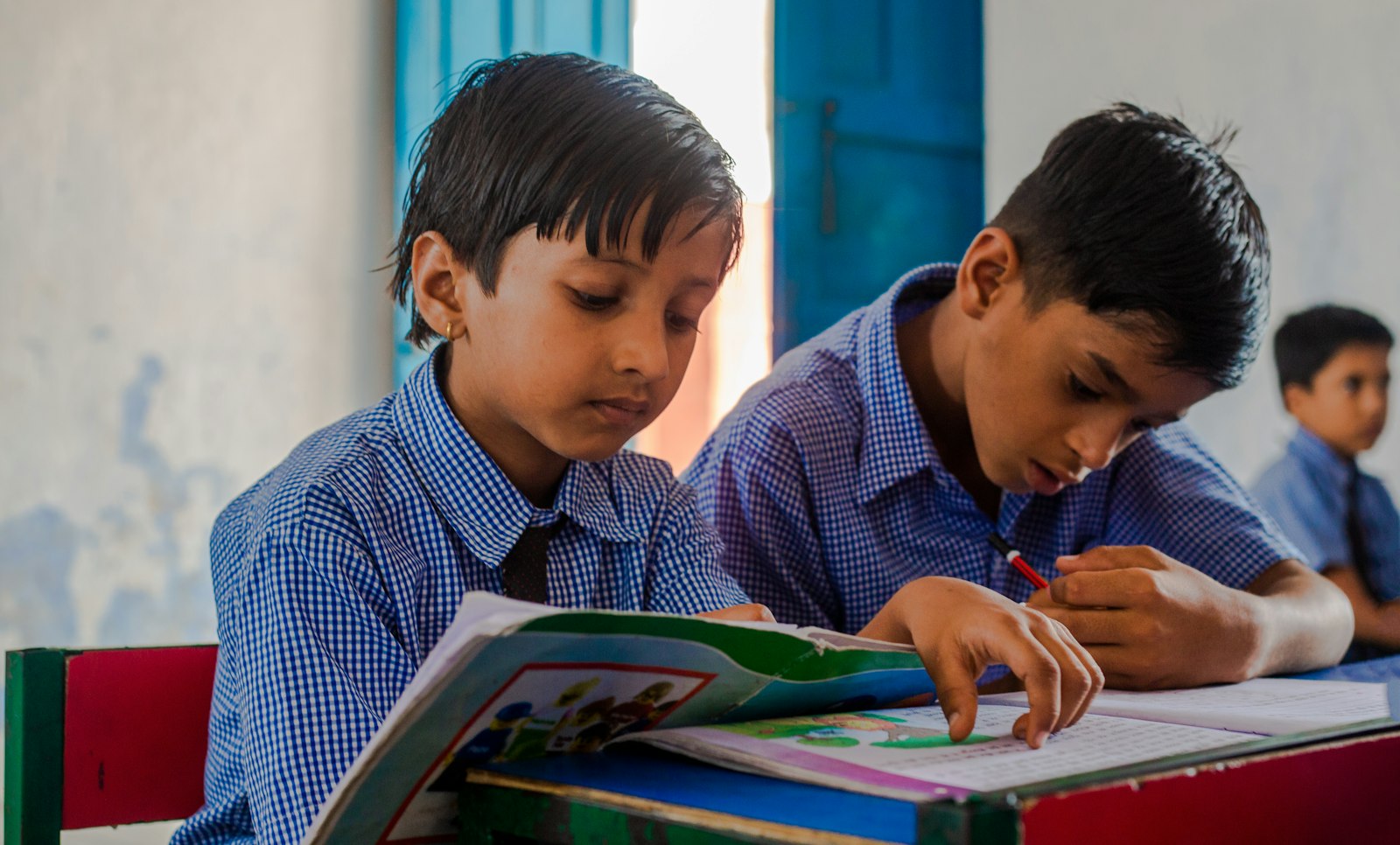 Two young boys sitting at a desk with a book